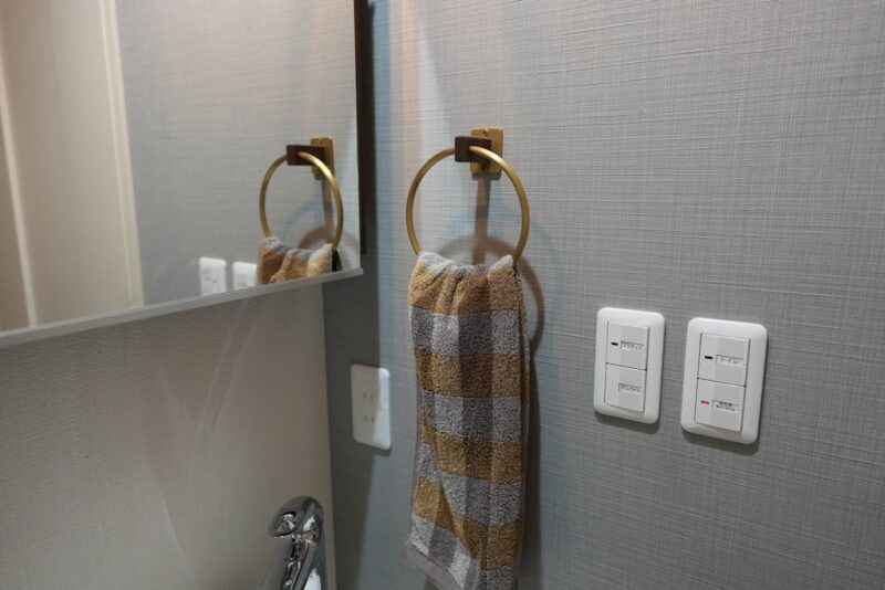 真鍮とオーク材を組み合わせたインターワークス製のタオルハンガー（D.Brass タオルハンガー）。洗面台の壁に取り付けられている様子。