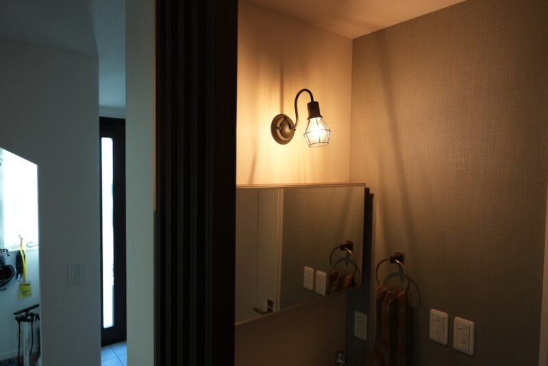 1階トイレ脇の洗面台に設置された、DAIKO製の木目調ブラケットライト（DBK-40813Y）。温かみのある電球色の明かり。