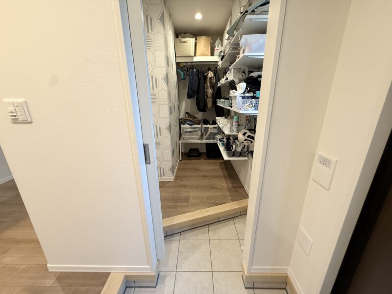 シューズクロークの内部。可動棚には靴やボックスが並び、ハンガーパイプにはコートが掛けられている。下部にはお掃除ロボットも設置されている。