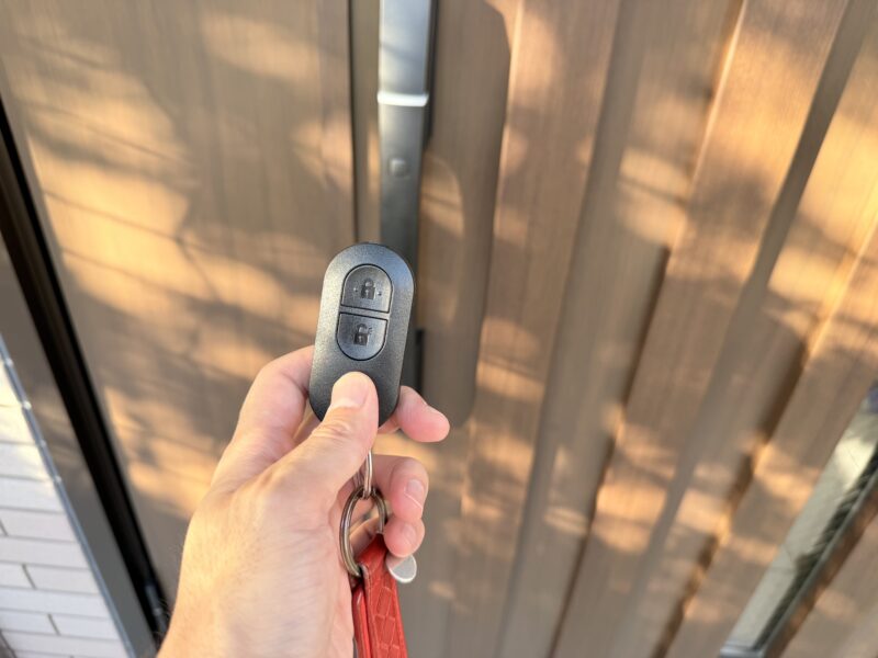 YKK APの玄関ドア前でスマートコントロールキー(リモコンキー)を手に持っている様子。