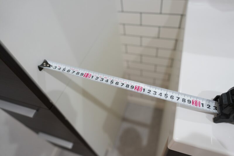セキスイハイムの洗面台横にある隙間にメジャーを当てて実測している写真。約27cm幅であることを示している画像